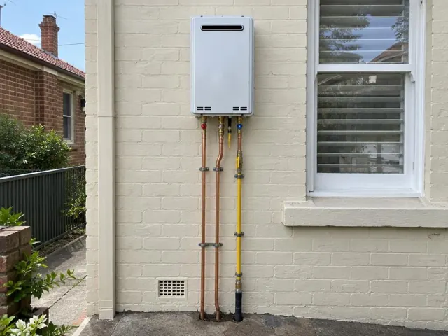 Wall-mounted hot water unit on a painted brick exterior wall beside a window in Bondi